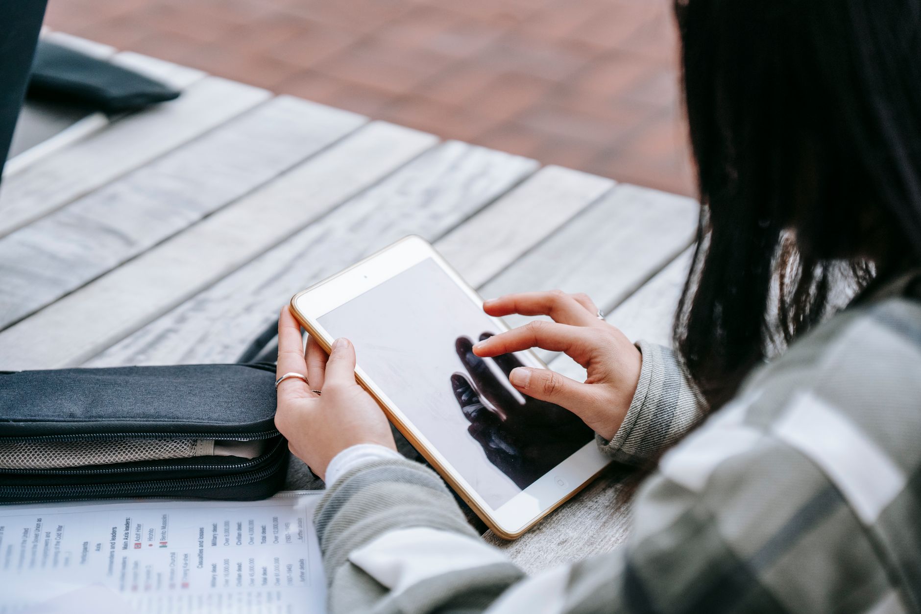 Woman at a wooden desk selects printable planner templates on a tablet while holding printed pages.