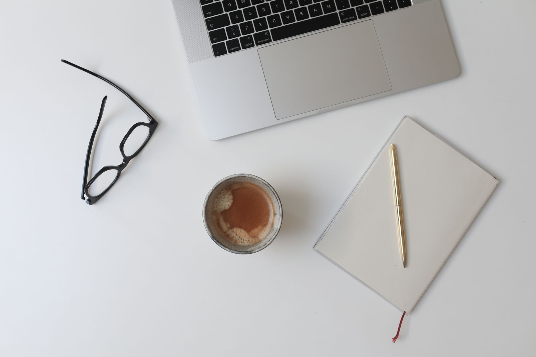 Neat minimal workspace with a laptop, notebook, and coffee cup on a white desk.