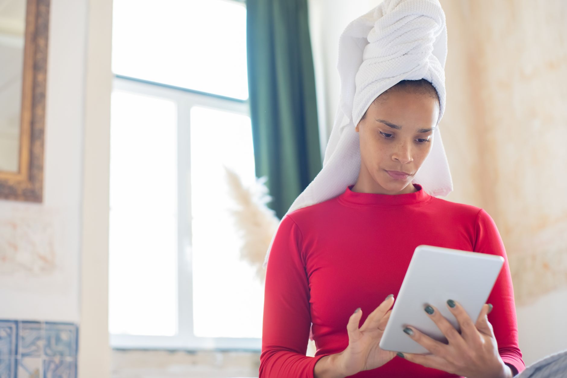 A woman sitting at a bright desk uses a tablet to browse digital printable wall art designs.