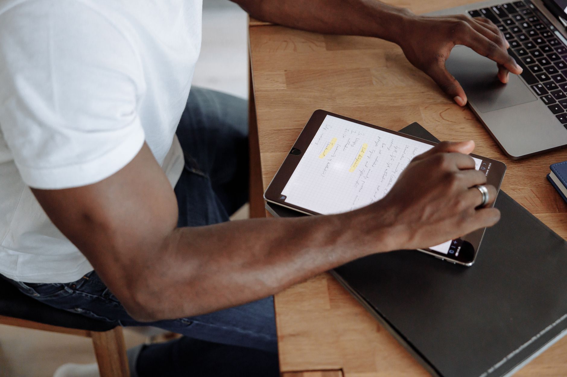 A person at a tidy home desk working on a laptop with a digital tablet and paper notebooks nearby