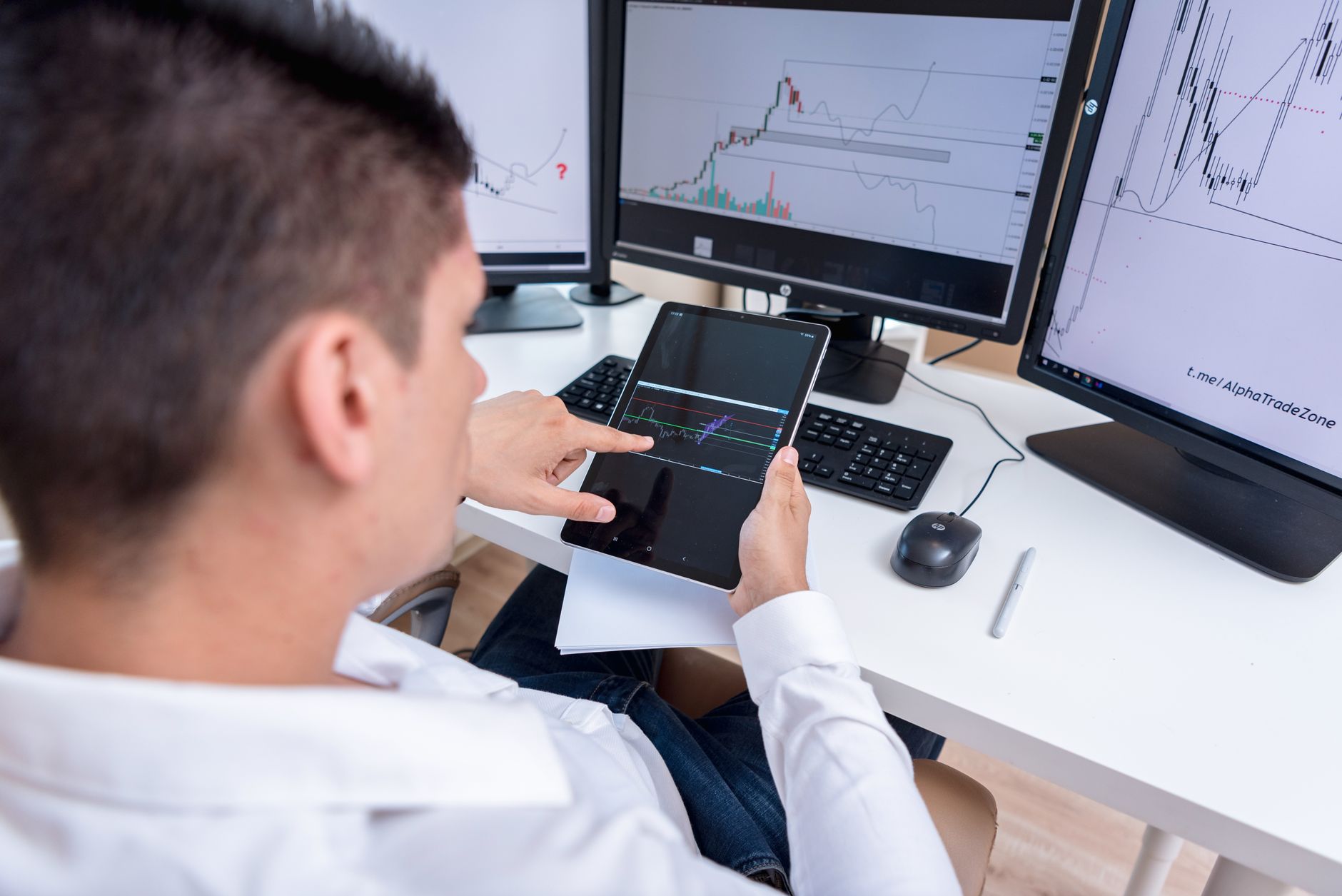 Investor looking at stock market charts on a tablet at a wooden desk