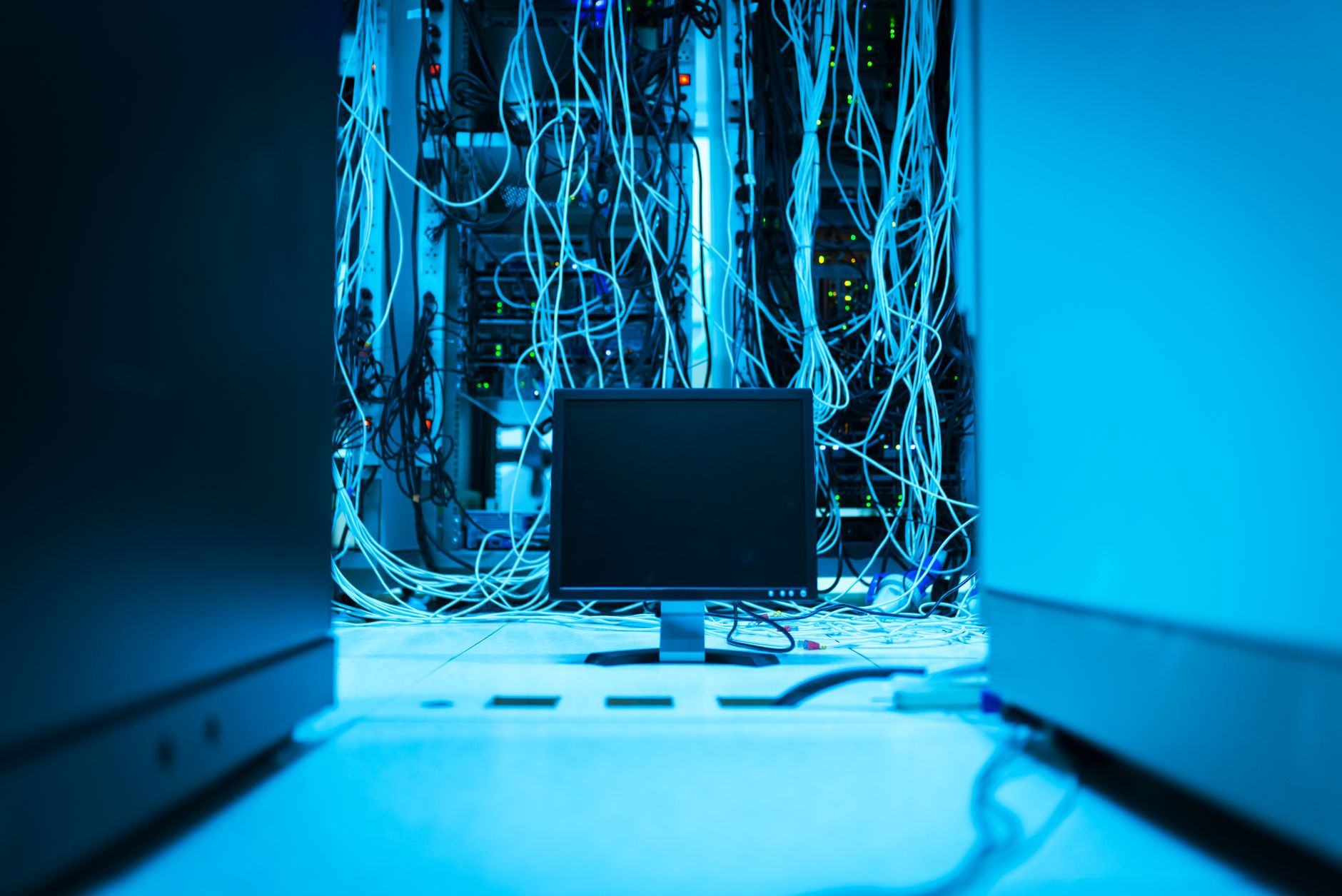Rows of server racks with blue and green lights and network cables in a dark data center