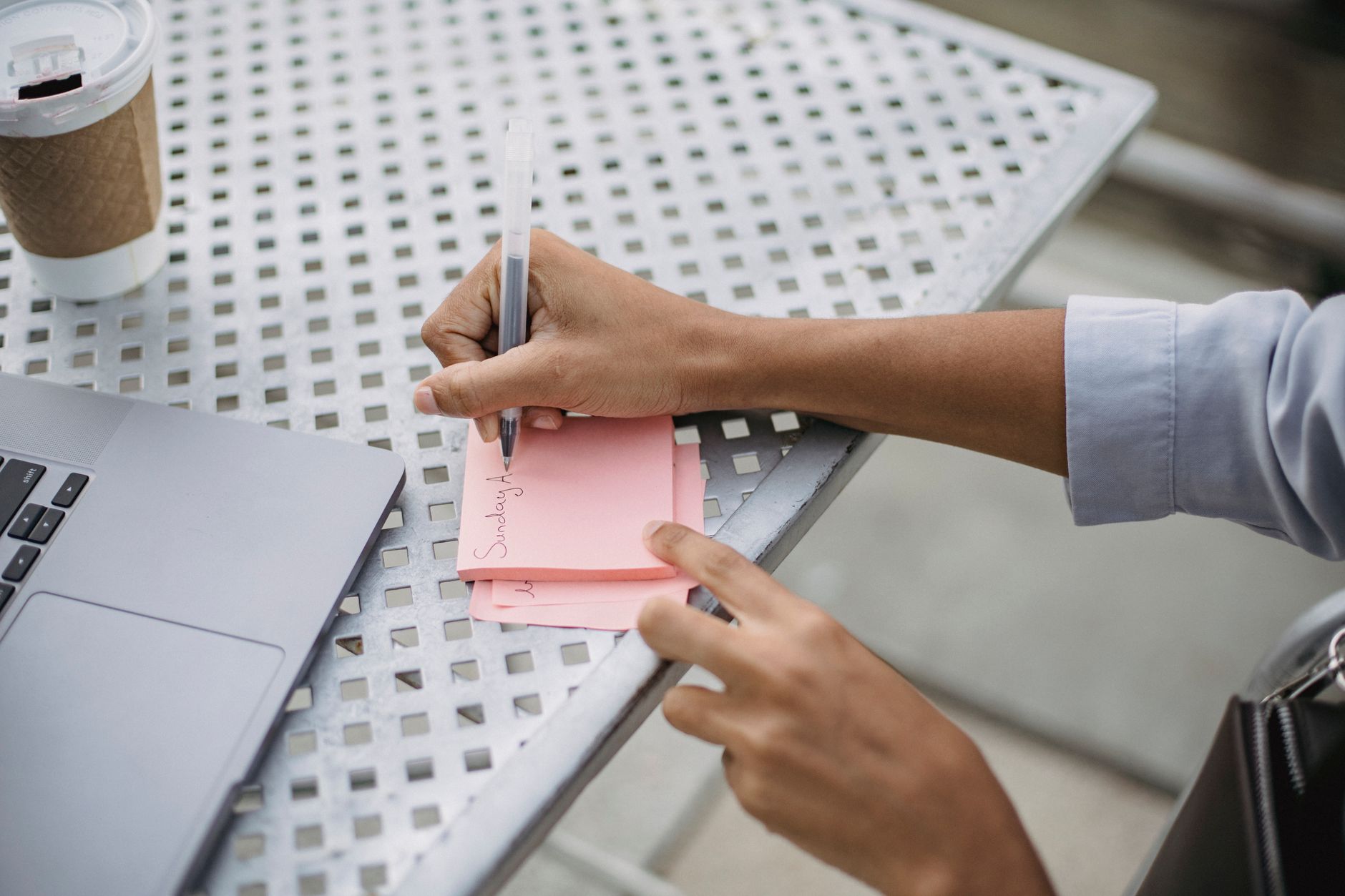 person writing notes next to a laptop and coffee while planning a product
